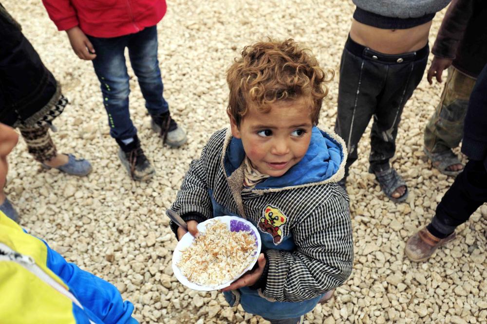 A displaced Syrian child, who fled their homes in Deir Ezzor city, eats a bowl of rice at a refugee camp in Syria’s northeastern Hassakeh province on February 26, 2018. / AFP / Delil souleiman