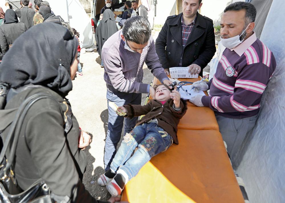 Syrian paramedics give medical attention to a girl after arriving on a convoy transporting civilians and rebel fighters to the village of Qalaat al-Madiq, about 45 kilometres northwest of the central city of Hama, on March 26, 2018 after their evacuation from Eastern Ghouta following a deal with the regime.  / AFP / OMAR HAJ KADOUR
