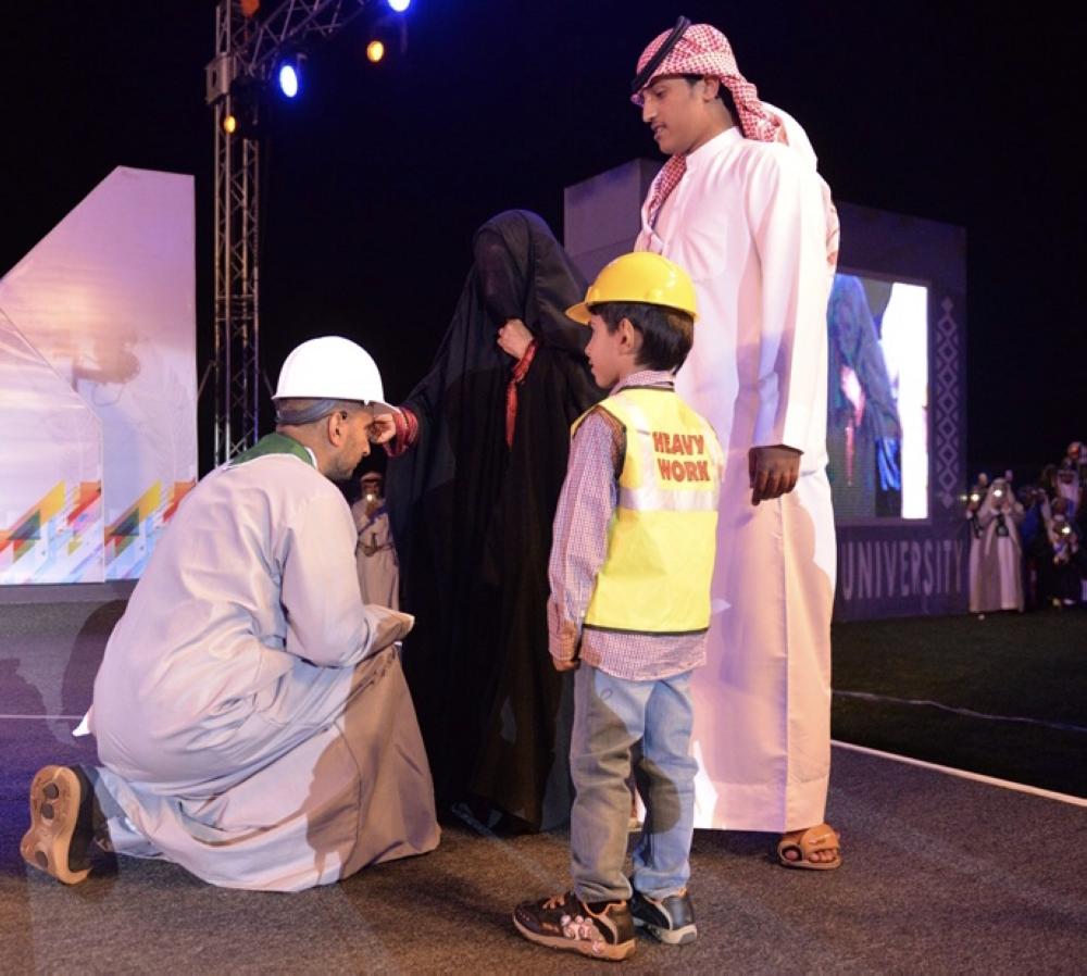 الخريج عون الشهراني منحنياً لوالدته أثناء تقليدها بردة التخرج له

