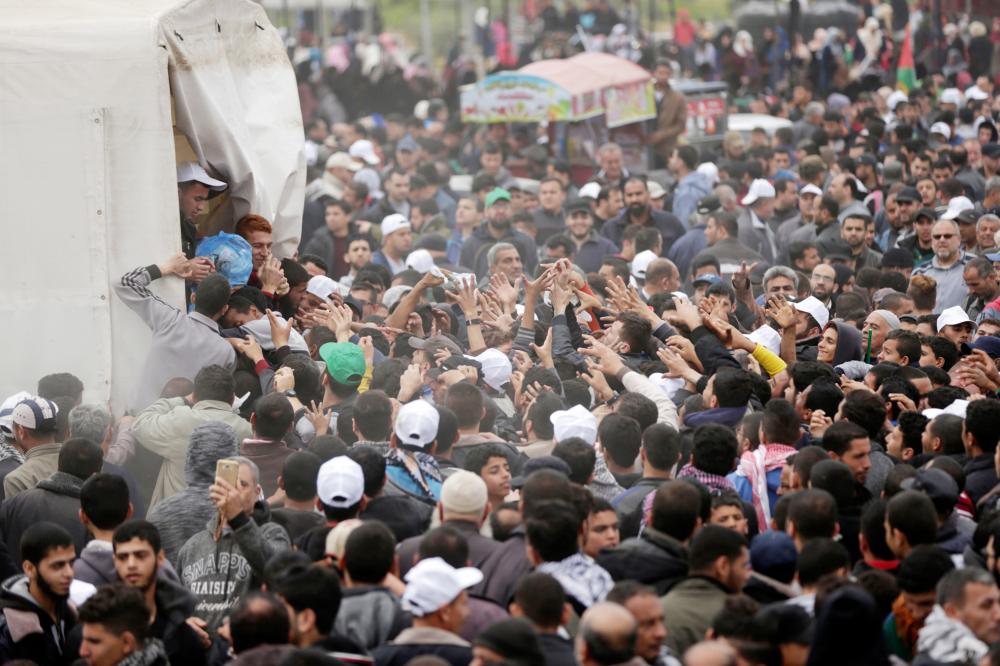 Palestinians gather to receive lunch packages after Friday prayers during a during a tent city protest near the border with Israel east of Gaza City to commemorate Land Day on March 30, 2018. Land Day marks the killing of six Arab Israelis during 1976 demonstrations against Israeli confiscations of Arab land. / AFP / MAHMUD HAMS
