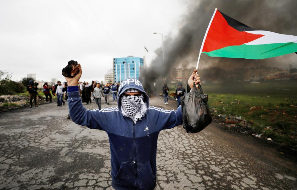 A demonstrator holds a Palestinian flag during clashes with Israeli troops at a protest marking Land Day, near Ramallah, in the occupied West Bank March 30, 2018. REUTERS/Mohamad Torokman