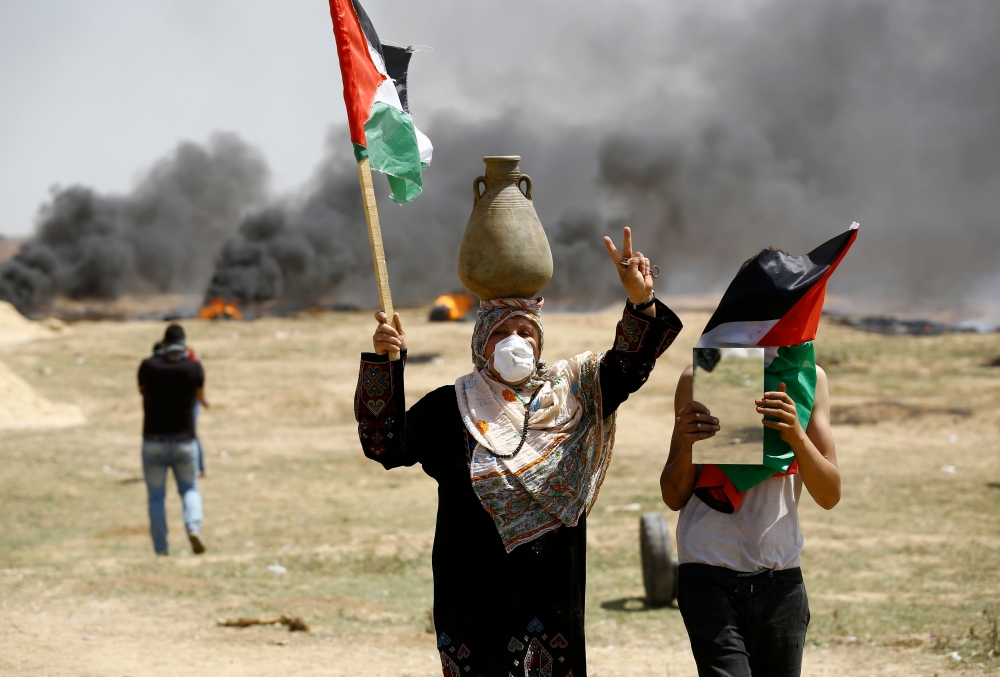 TOPSHOT - A Palestinian man waves his national flag as others burn tyres to protect themselves from shots of Israeli soldiers during a protest at the Israel-Gaza border, east of Jabalia, northern Gaza Strip on April 6, 2018. Clashes erupted on the Gaza-Israel border on April 6, AFP journalists said, a week after similar demonstrations led to violence in which Israeli force killed 19 Palestinians, the bloodiest day since a 2014 war.
 / AFP / MOHAMMED ABED
