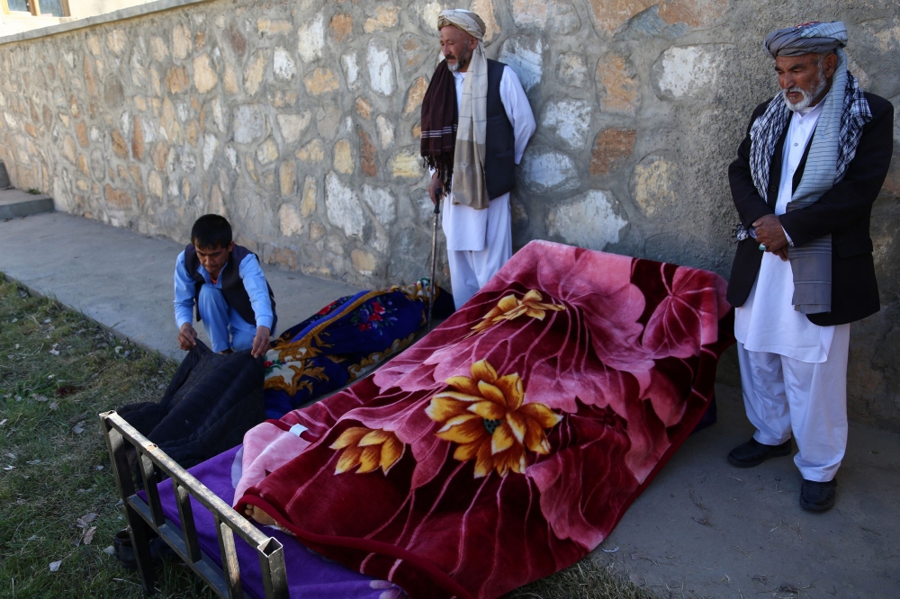 Afghan men stand over dead bodies at the site of an attack by Taliban militants on a government compound in the Khwaja Omari district in the southeastern province of Ghazni on April 12, 2018. Taliban militants launched a pre-dawn raid on a district government compound in Afghanistan on April 12, killing at least seven people including the local governor, officials said. / AFP / ZAKERIA HASHIMI
