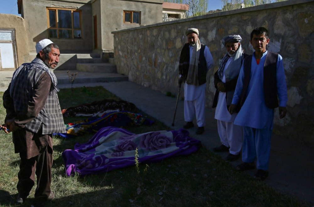 Afghan men stand over dead bodies at the site of an attack by Taliban militants on a government compound in the Khwaja Omari district in the southeastern province of Ghazni on April 12, 2018. Taliban militants launched a pre-dawn raid on a district government compound in Afghanistan on April 12, killing at least seven people including the local governor, officials said. / AFP / ZAKERIA HASHIMI
