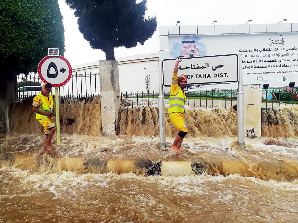 عمال نظافة يحاولون فتح المناهل لتصريف المياه المتجمعة في الشوارع. (تصوير: يحيى الفيفي)