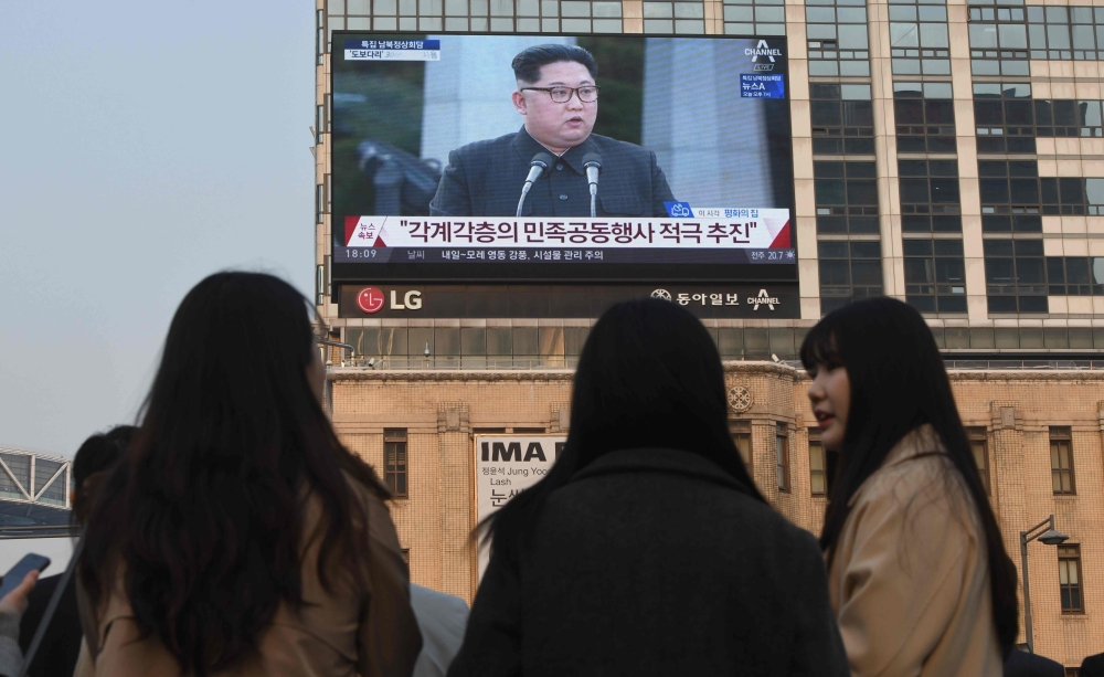 Pedestrians walk cross the road as a big screen shows live footage of a joint press conference between South Korean President Moon Jae-in and North Korean leader Kim Jong Un during the inter-Korean summit, in downtown Seoul on April 27, 2018. The leader of nuclear-armed North Korea Kim Jong Un and the South's President Moon Jae-in said they were committed to the denuclearisation of the Korean peninsula after a historic summit on April 27.
 / AFP / afp / Jung Yeon-je
