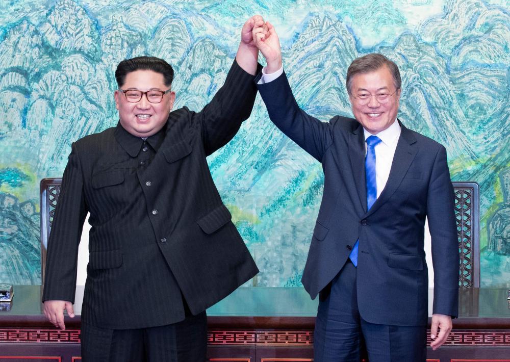 TOPSHOT - North Korea's leader Kim Jong Un (L) and South Korea's President Moon Jae-in (R) raise their jointed hands during a signing ceremony near the end of their historic summit at the truce village of Panmunjom on April 27, 2018. The leaders of South and North Korea embraced warmly after signing a statement in which they declared 