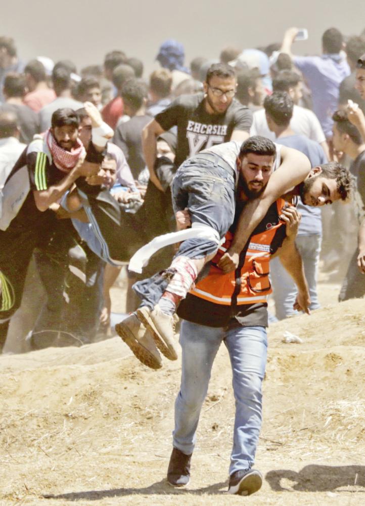 A Palestinian man carries an injured man during clashes with Israeli forces near the border between the Gaza strip and Israel east of Gaza City on May 14, 2018, as Palestinians protest over the inauguration of the US embassy following its controversial move to Jerusalem. Dozens of Palestinians were killed by Israeli fire on May 14 as tens of thousands protested and clashes erupted along the Gaza border against the US transfer of its embassy to Jerusalem, after months of global outcry, Palestinian anger and exuberant praise from Israelis over President Donald Trump's decision tossing aside decades of precedent. / AFP / MAHMUD HAMS
