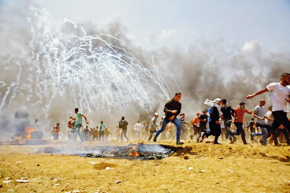 Palestinians run for cover from tear gas during clashes with Israeli security forces near the border between Israel and the Gaza Strip, east of Jabalia on May 14, 2018, as Palestinians protest over the inauguration of the US embassy following its controversial move to Jerusalem.  / AFP / MOHAMMED ABED
