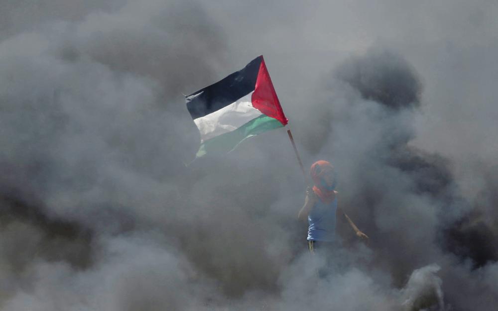 A boy holds a Palestinian flag as he stands amidst smoke during a protest against U.S. embassy move to Jerusalem and ahead of the 70th anniversary of Nakba, at the Israel-Gaza border east of Gaza City May 14, 2018. REUTERS/Mohammed Salem