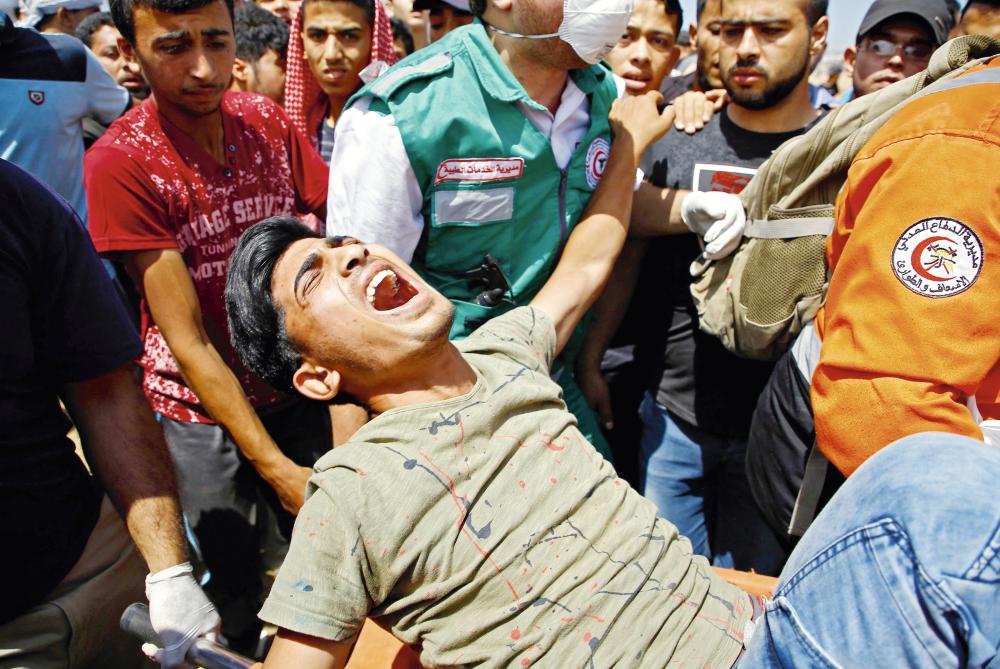 Emergency services and Palestinians carry a wounded protestor during clashes with Israeli security forces near the border between Israel and the Gaza Strip, east of Jabalia on May 14, 2018, as Palestinians protest over the inauguration of the US embassy following its controversial move to Jerusalem.  / AFP / MOHAMMED ABED
