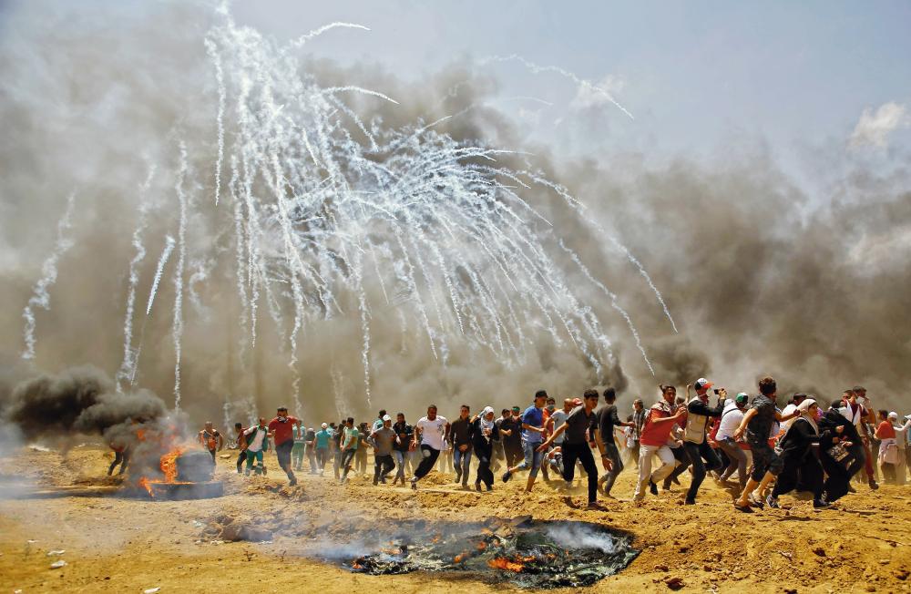 TOPSHOT - Palestinians run for cover from tear gas during clashes with Israeli security forces near the border between Israel and the Gaza Strip, east of Jabalia on May 14, 2018, as Palestinians protest over the inauguration of the US embassy following its controversial move to Jerusalem.  / AFP / MOHAMMED ABED
