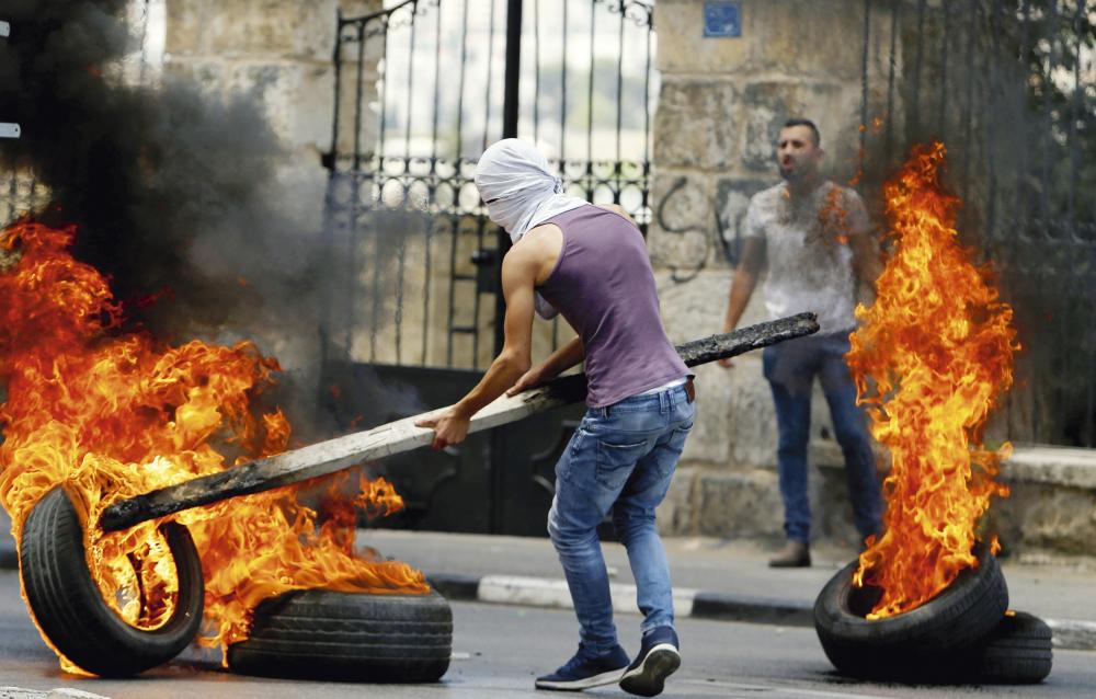 A Palestinian demonstrator moves a burning tire during a protest against U.S. embassy move to Jerusalem and ahead of the 70th anniversary of Nakba, in Bethlehem in the occupied West Bank May 14, 2018. REUTERS/Mussa Qawasma