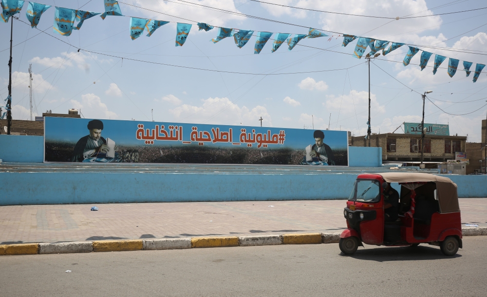 A small vehicle drives past a poster of Shiite leader Moqtada al-Sadr in Sadr City, east of the Iraqi capital Baghdad on May 14, 2018. In the impoverished stronghold of Iraqi cleric Moqtada Sadr in Baghdad, supporters of the Shiite populist are hopeful for improvements as results put him on top in parliament elections.  / AFP / AHMAD AL-RUBAYE
