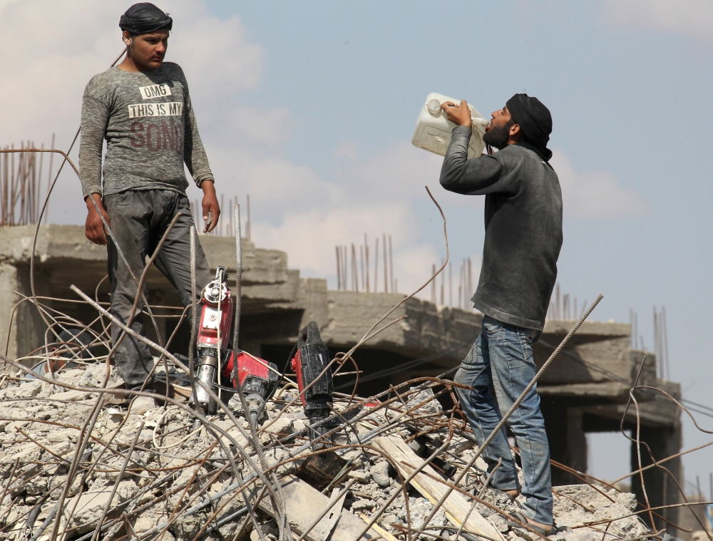 A worker drinks water from a container as he stands on rubble of damaged buildings in Raqqa, Syria May 14, 2018. REUTERS/Aboud Hamam