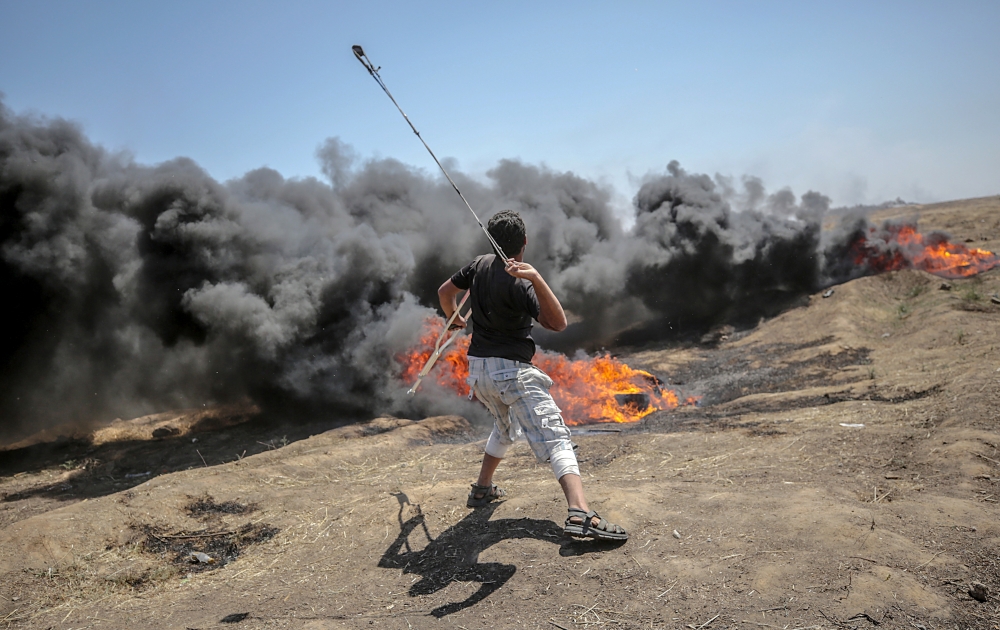 epaselect epa06737561 A Palestinian protester throws stones during clashes after protests near the border with Israel in the east of Gaza Strip, 14 May 2018 (issued 15 May 2018). More protests are expected in the Palestinian territories on 15 May. At least 58 Palestinian protesters were killed and more than 2,000 others were injured at the Gaza-Israeli border during clashes against the US embassy move to Jerusalem as well as marking the Nakba Day. Palestinians are marking the Nakba Day, or the day of the disaster, when more than 700 thousand Palestinians were forcefully expelled from their villages during the war that led to the creation of the state of Israel on 15 May 1948. Protesters call for the right of Palestinians to return to their homeland. EPA/MOHAMMED SABER