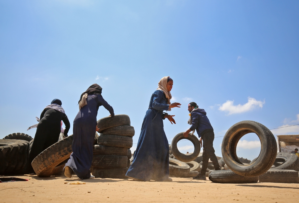 Palestinian men and women pile up tires in a make-shift barricade before burning them during demonstrations near the border with Israel, east of Khan Yunis in the southern Gaza Strip on May 15, 2018, marking 70th anniversary of Nakba -- also known as Day of the Catastrophe in 1948 -- and against the US' relocation of its embassy from Tel Aviv to Jerusalem.  / AFP / SAID KHATIB
