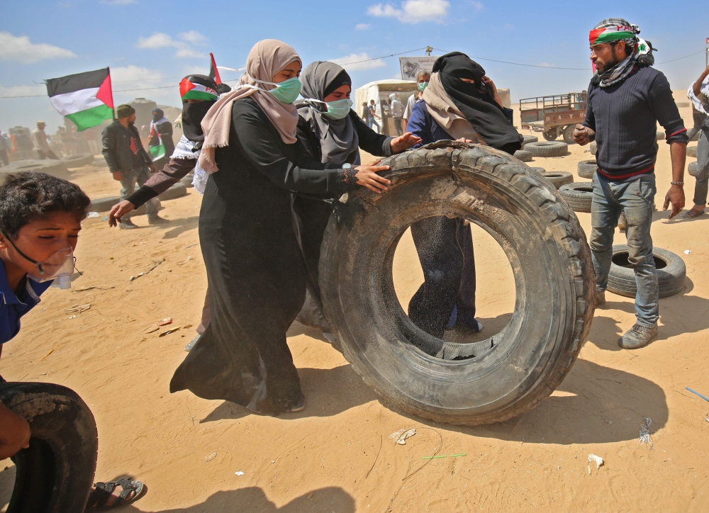 Palestinian women roll a tire towards a make-shift barricade before burning them during demonstrations near the border with Israel, east of Khan Yunis in the southern Gaza Strip on May 15, 2018, marking 70th anniversary of Nakba -- also known as Day of the Catastrophe in 1948 -- and against the US' relocation of its embassy from Tel Aviv to Jerusalem.  / AFP / SAID KHATIB
