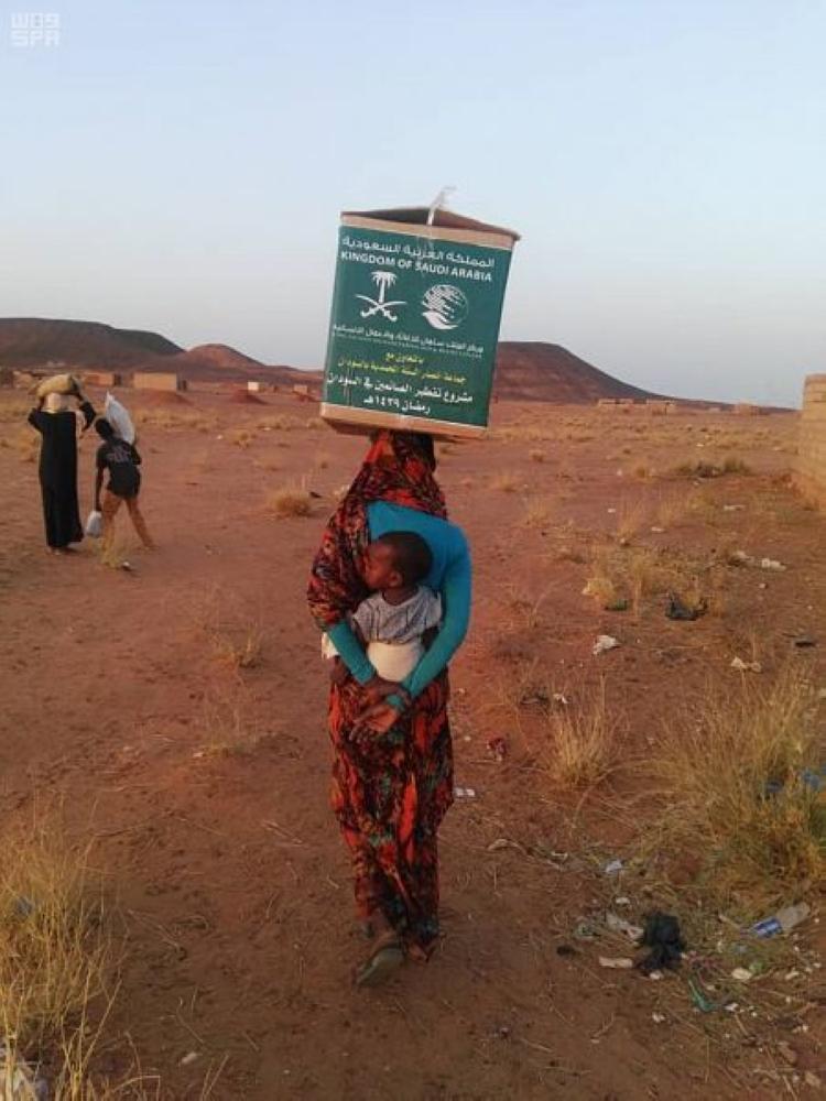 سودانية تحمل على رأسها صندوق إغاثة من مركز الملك سلمان. (عكاظ)