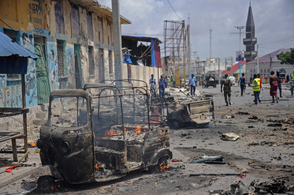 Bystanders and rescue personnel look on as the wreckage of a vehicle burns at the site of a car bomb explosion near the building of the Interior Ministry in Mogadishu on July 7, 2018. Two explosions have rocked Somalia's internal security ministry in the capital Mogadishu, killing five civilians, a police officer said, in the latest attack claimed by Shabaab militants. / AFP / Mohamed ABDIWAHAB               
