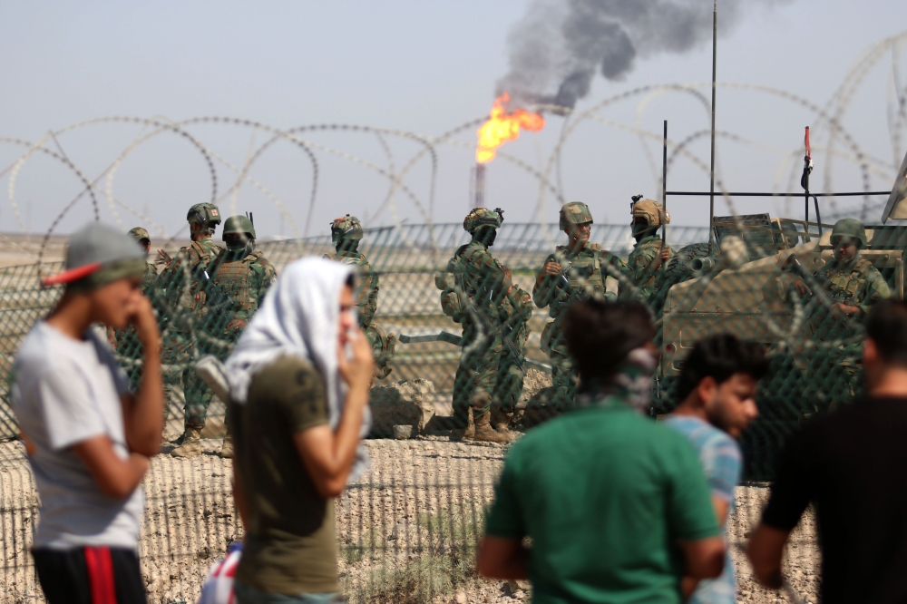 Protesters demonstrate as Iraqi soldiers stand guard oil fields in al-Qurnah, some 100 kilometers north of Basra, southern Iraq, on July 14, 2018. Iraqi Prime Minister Haider al-Abadi sought on July 14 to restore calm in the city of Basra after days of protests over unemployment, as demonstrations spread to other regions. / AFP / Haidar MOHAMMED ALI
