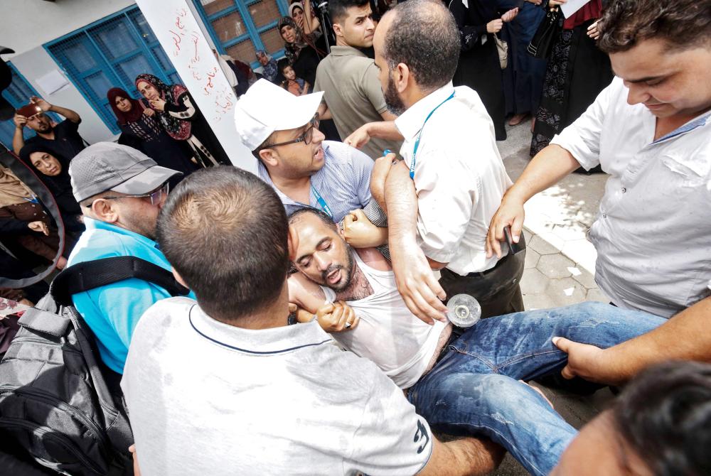 Palestinians help an employee of the United Nations agency for Palestinian refugees UNRWA  who reportedly tried to set himself on fire as fellow employees take part in a protest against job cuts announced by the agency, at its headquarters in Gaza City July 25, 2018. UNRWA announced today that it was cutting more than 250 jobs in the Palestinian territories after the United States held back hundreds of millions in aid.  / AFP / SAID KHATIB
