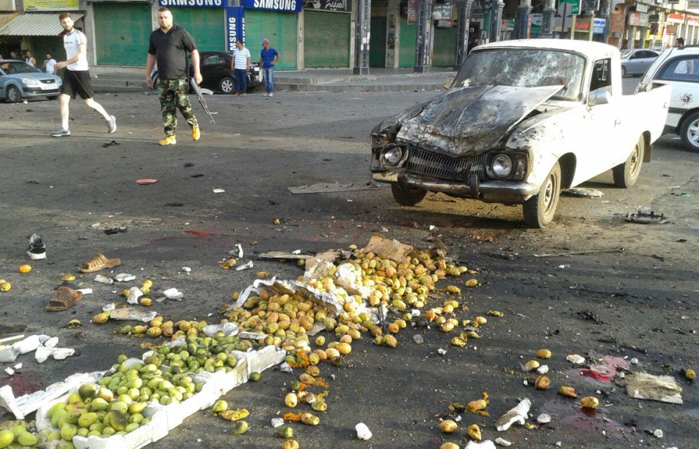 A handout picture released by the official Syrian Arab News Agency (SANA) on July 25, 2018 shows a member of the Syrian security forces walking past a truck damaged in a suicide attack in the southern city of Sweida.  A string of suicide attacks in Syria by the Islamic State (IS) group has killed at least 40 people, mostly pro-regime fighters, in one of the jihadists' deadliest operations in months, a war monitor said today.  - XGTY / XGTY /  == RESTRICTED TO EDITORIAL USE - MANDATORY CREDIT 