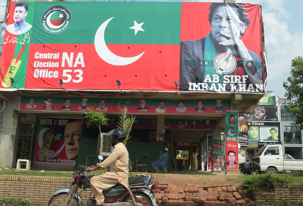 A Pakistani motorcyclist rides past a billboard featuring an image of Pakistan's cricketer-turned politician Imran Khan, head of the Pakistan Tehreek-e-Insaf (Movement for Justice) party, a day after the general election in Islamabad on July 26, 2018. Pakistan woke to electoral chaos on July 26 with the outgoing ruling party denouncing «blatant rigging» in the pivotal general election and rejecting unofficial, partial results suggesting victory for former cricket champion Imran Khan. / AFP / AAMIR QURESHI
