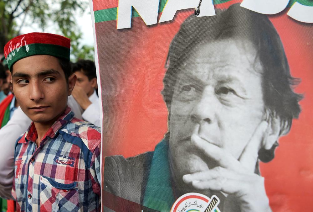 A supporters of Pakistan's cricketer-turned politician and head of the Pakistan Tehreek-e-Insaf (Movement for Justice) party Imran Khan stands next to poster with a picture of Khan as they gather near his residence in Islamabad on July 26, 2018. Pakistan cricket hero turned politician Imran Khan claimed victory on July 26 in the country's tense general election marred by allegations of 