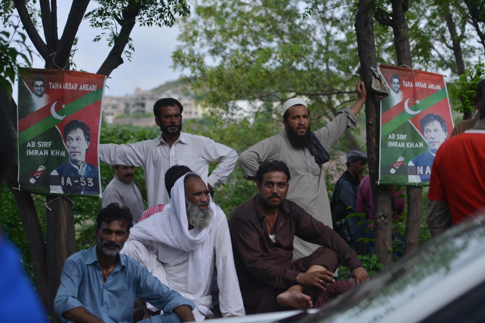 TOPSHOT - Supporters of Pakistan's cricketer-turned politician Imran Khan, and head of the Pakistan Tehreek-e-Insaf (Movement for Justice) party, sit next to posters featuring images of Khan's as they gather near his residence in Islamabad on July 26, 2018, a day after the general election. Pakistan cricket hero turned politician Imran Khan claimed victory on July 26 in the country's tense general election marred by allegations of «blatant» rigging by rival parties. A visibly tired Khan cut a conciliatory tone in a wide-ranging address to the nation following a controversial contest hit by accusations from major political parties of poll rigging and long delays in still unreleased official results. / AFP / AAMIR QURESHI
