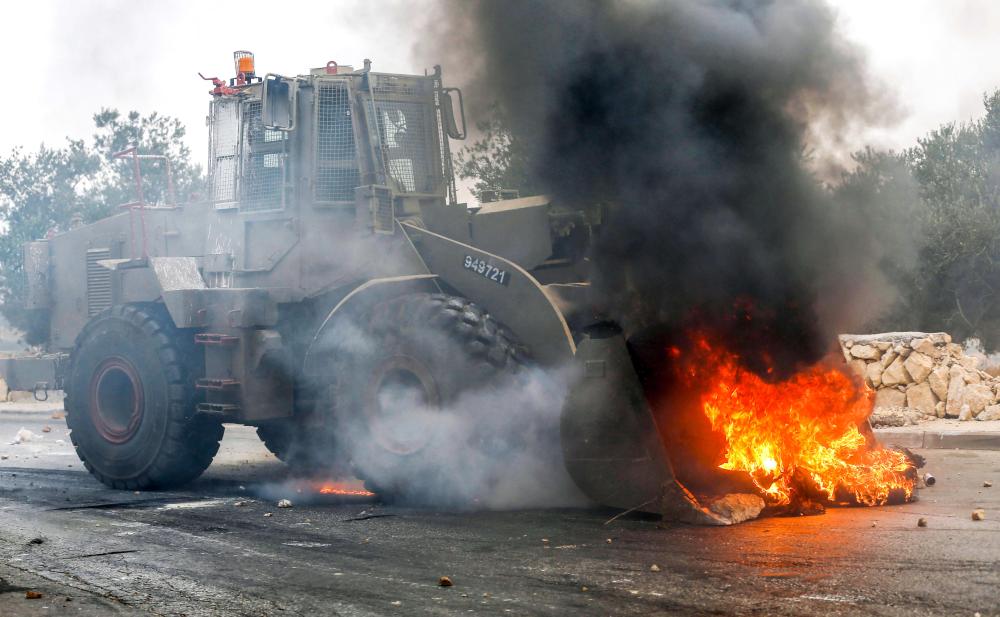 An Israeli bull dozer clears flaming tires from a road during clashes in the village of Kobar, west of Ramallah in the occupied West Bank on July 27, 2018, where a Palestinian stabbing attacker left from the previous night towards the Adam settlement. The knife attack by a 17-year-old Palestinian killed one Israeli and wounded two others, while the assailant was shot dead, Israeli authorities said. A 58-year-old victim was said to be seriously wounded but stable. The third victim, who also shot the Palestinian, was slightly wounded in the leg. / AFP / ABBAS MOMANI
