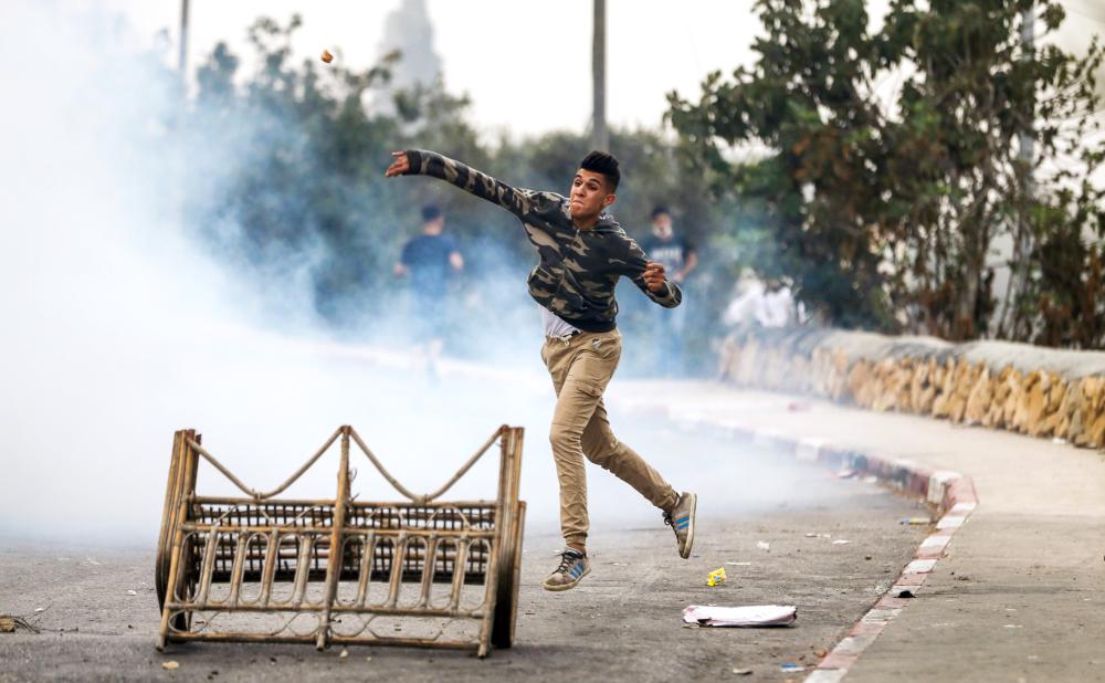 A Palestinian protester throws stones at Israeli security forces during clashes in the village of Kobar, west of Ramallah in the occupied West Bank on July 27, 2018, where a Palestinian stabbing attacker left from the previous night towards the Adam settlement. The knife attack by a 17-year-old Palestinian killed one Israeli and wounded two others, while the assailant was shot dead, Israeli authorities said. A 58-year-old victim was said to be seriously wounded but stable. The third victim, who also shot the Palestinian, was slightly wounded in the leg. / AFP / ABBAS MOMANI
