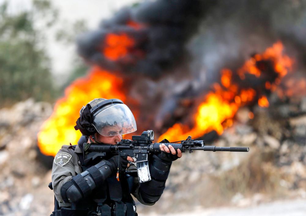 



 جندي إسرائيلي يطلق النار على متظاهرين فلسطينيين في رام الله بالضفة الغربية المحتلة أمس.  (أ ف ب)