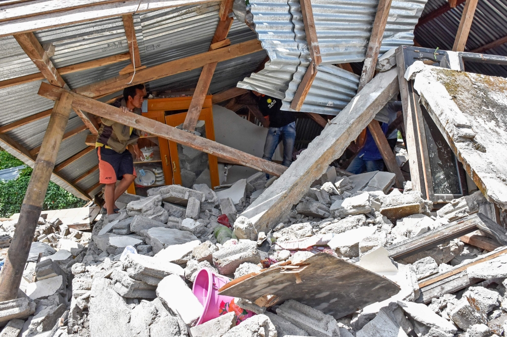 An Indonesian man looks at the remains of a house, after a 6.4 magnitude earthquake struck, in Lombok on July 29, 2018. A powerful earthquake on the Indonesian tourist island of Lombok killed at least 13 people, injured hundreds and damaged thousands of homes on July 29, officials said. / AFP / AULIA AHMAD
