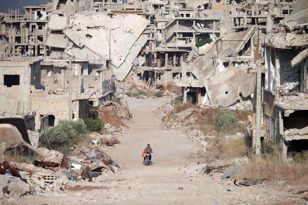 TOPSHOT - A picture taken on August 2, 2018, shows a man riding a motorcycle past destroyed buildings in the opposition-held southern city of Daraa. / AFP / Mohamad ABAZEED
