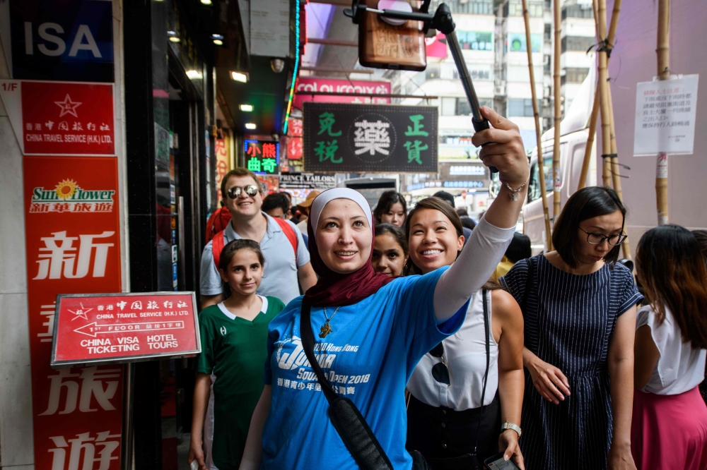 n this photo taken on August 2, 2018, Squash Dreamers team coach Reem Niaz (C), a refugee from Damascus, takes a selfie with Squash Dreamers executive director Clayton Kier (back L), Squash Dreamers vice president Rachel Lee (centre R) and Syrian squash players Sabah Husryeh, 11 (centre L) and her sister Raghda Husryeh (back centre R), 13, as they look for an shop that sells tea in the Kowloon district of Hong Kong. Three young Syrian squash players, aged between 11 and 13, are part of a new team called Squash Dreamers, made up of displaced Syrian youngsters who were forced to flee their war-torn homeland. - TO GO WITH HongKong-Syria-sport-squash-refugee by Yan ZHAO
 / AFP / Anthony WALLACE / TO GO WITH HongKong-Syria-sport-squash-refugee by Yan ZHAO
