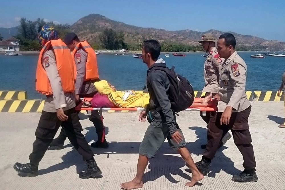 This handout picture taken on August 6, 2018 and released by Indonesia Water Police shows rescuers carrying an injured person as hundreds of people leave Gili Trawangan, north of neighbouring Lombok island, a day after a 6.9 magnitude earthquake struck the area. More than 1,000 tourists were being evacuated from Indonesia's tiny Gili islands on August 6 after a powerful quake struck neighbouring Lombok, killing 91 people and injuring hundreds. - -----EDITORS NOTE --- RESTRICTED TO EDITORIAL USE - MANDATORY CREDIT 