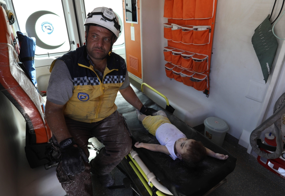 EDITORS NOTE: Graphic content / A Syrian rescue worker, part of the White Helmets team, sits next to the body of a baby inside an ambulance on August 12, 2018 following an explosion at an arms depot in a residential area in Syria's northern Idlib province city of Sarmada in which 12 people were reportedly killed. / AFP / OMAR HAJ KADOUR
