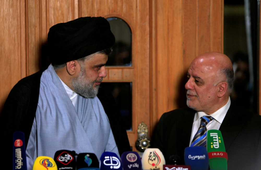 FILE PHOTO: Iraqi Shi'ite cleric Moqtada al-Sadr, who's bloc came first, looks at Iraqi Prime Minister Haider al-Abadi, who's political bloc came third in a May parliamentary election, during a news conference in Najaf, Iraq June 23, 2018. REUTERS/Alaa al-Marjani/ File Photo