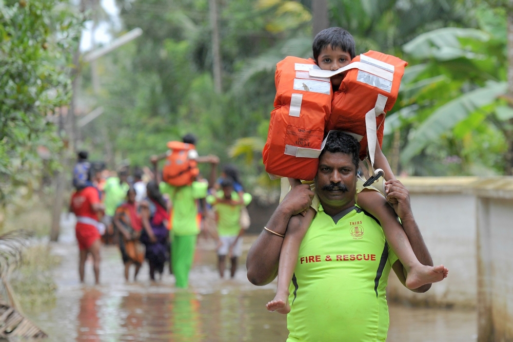 TOPSHOT - Kerala and Tamil Nadu Fire Force personnel carry children on their shoulders through flood waters during a rescue operation in Annamanada village in Thrissur District, in the south Indian state of Kerala, on August 19, 2018. Rescuers waded into submerged villages in southern India on August 19 in a desperate search for survivors cut off for days by floods that have already killed more than 350 people.
 / AFP / MANJUNATH KIRAN
