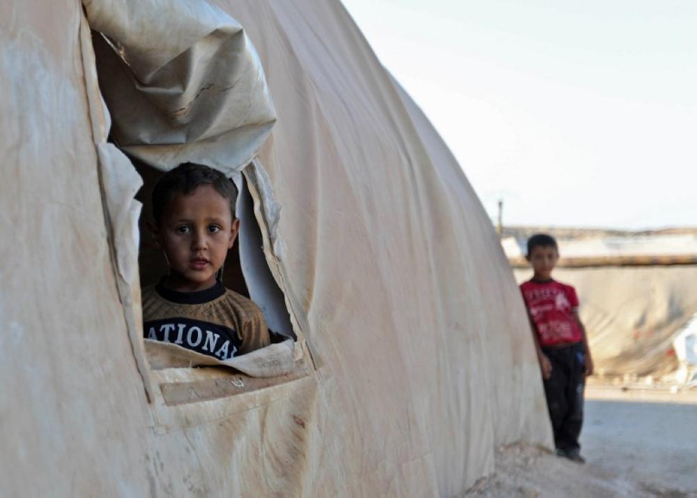 A young boy peeks out of a tent in a camp for the displaced from the south of Idlib province and the north of Hama province, in Kafr Dariyan situated at a short distance from Syria's border with Turkey, on August 26, 2018. / AFP PHOTO / OMAR HAJ KADOUR