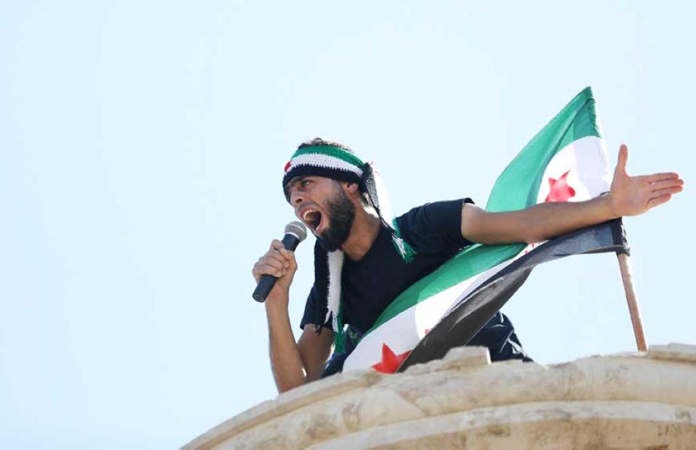 A Syrian protester wearing the colours of opposition shouts slogans in a microphone during an anti-government demonstration in the rebel-held town of Maaret al-Numan, in the north of Idlib province on September 28, 2018. / AFP / OMAR HAJ KADOUR
