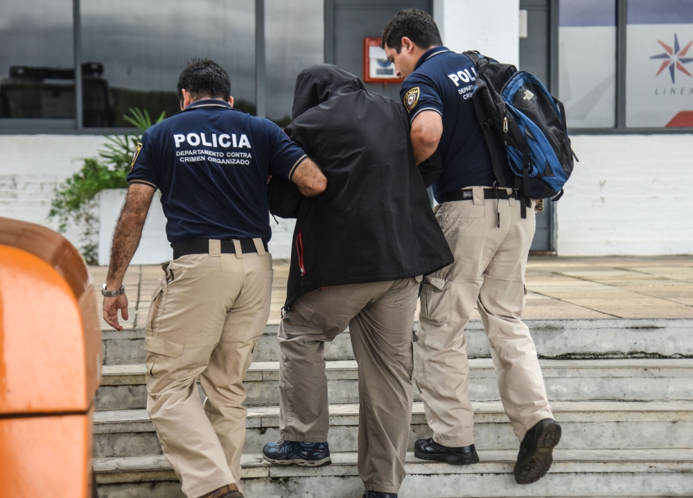 TOPSHOT - Iranian pilot, Nader Ali Saboori Haghighi (C), is arrested by the Paraguayan members of the organised crime police, for carrying illegal identity and air navigation documents, at the Silvio Pettirossi airport, in Luque, Paraguay on October 13, 2018. Nader Ali Saboori Haghighi, was sentence for identity fraud in US on 2015. / AFP / NORBERTO DUARTE 