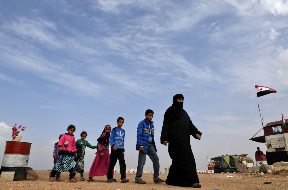 TOPSHOT - Syrian families walk as members of Russian and Syrian forces stand guard at the Abu Duhur crossing on the eastern edge of Syria's Idlib province on October 23, 2018. Civilians are coming from rebel-held areas in Idlib province and entering regime-held territories through the Abu Duhur crossing, some of them returning to their villages that were recaptured by the regime forces earlier this year. / AFP / GEORGE OURFALIAN 