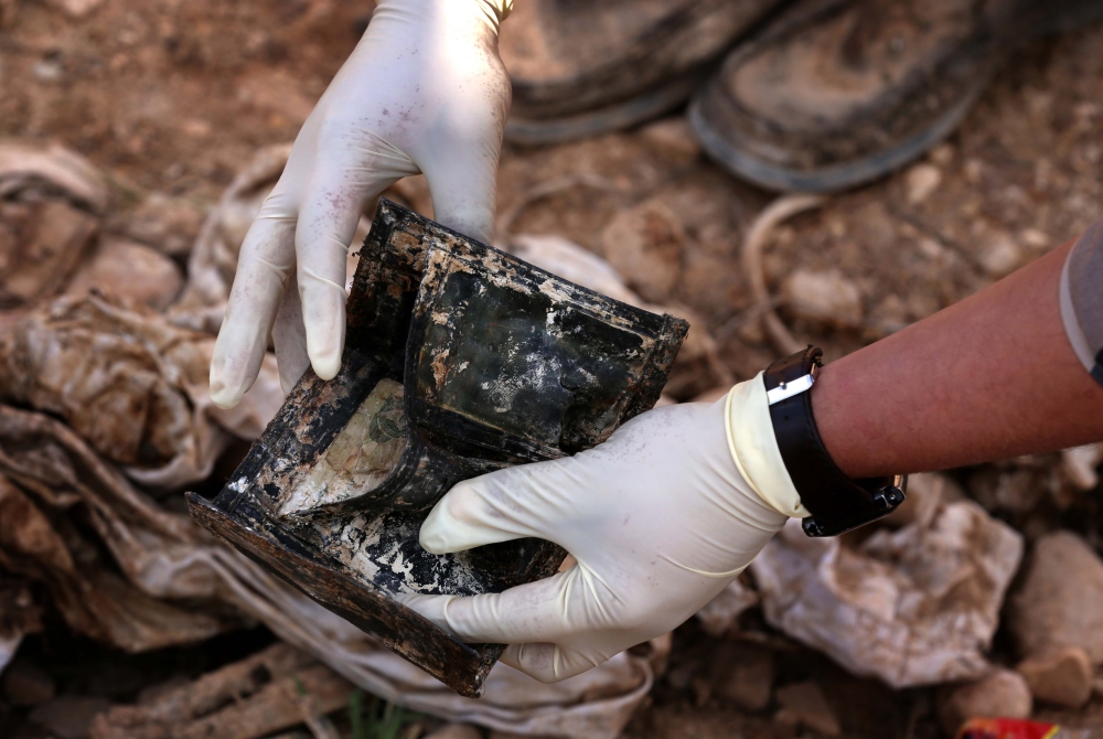 (FILES) In this file photo taken on February 03, 2015 a member of the Yazidi minority searches in a wallet for clues, that might lead him to missing relatives in the remains of people killed by the Islamic State (IS) jihadist group, a day after Kurdish forces discovered a mass grave near the Iraqi village of Sinuni, in the northwestern Sinjar area.  The Islamic State group left behind more than 200 mass graves in Iraq containing up to 12,000 victims that could hold vital evidence of war crimes, the UN said November 6, 2018.
The United Nations in Iraq (UNAMI) and its human rights office said they had documented a total of 202 mass graves in parts of western and northern Iraq held by IS between 2014 and 2017. / AFP / Safin HAMED
