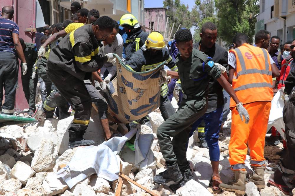 TOPSHOT - Emergency rescue staff carry the body of a victim over rubble at the scene of a car-bomb attack on February 4, 2019 in Somalia capital Mogadishu's Hamarwayne District. At least nine people were killed and several wounded when a car loaded with explosives blew up near a mall in a busy market in the Somali capital on Monday, police said. / AFP / ABDIRAZAK HUSSEIN FARAH 