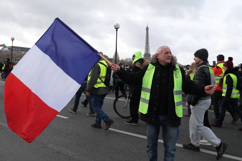 A protester holds the French national flag during a demonstration in Paris on February 9, 2019, as 'Yellow Vest' protesters (Gilets Jaunes) take to the streets for 13th consecutive Saturday. / AFP / Zakaria ABDELKAFI 