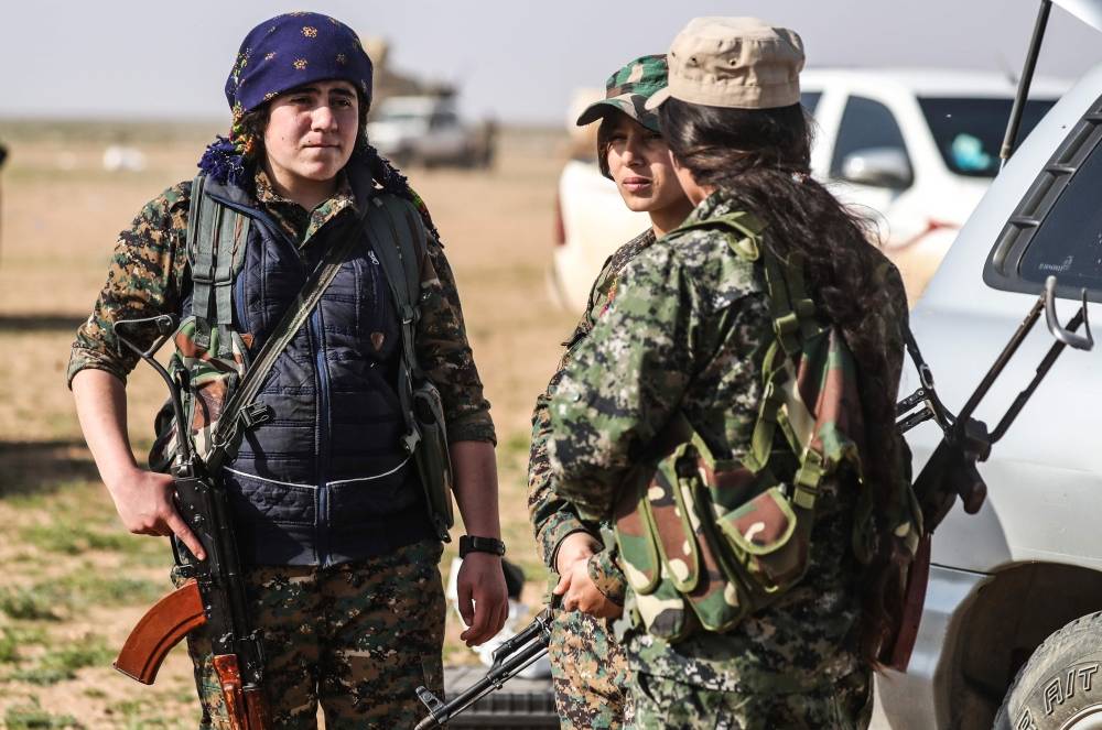 Fighters with the US-backed Syrian Democratic Forces (SDF) gather at a scanning area for people who are evacuated from the Islamic State (IS) group's embattled holdout of Baghouz, during an operation to expel IS jihadists from the area, in the eastern Syrian province of Deir Ezzor, on February 25, 2019. US-backed forces evacuated over 40 truckloads of people from the Islamic State group's last Syria redoubt today, as they sought to clear out civilians before a final push to crush the jihadists. / AFP / Delil souleiman AND Delil SOULEIMAN 