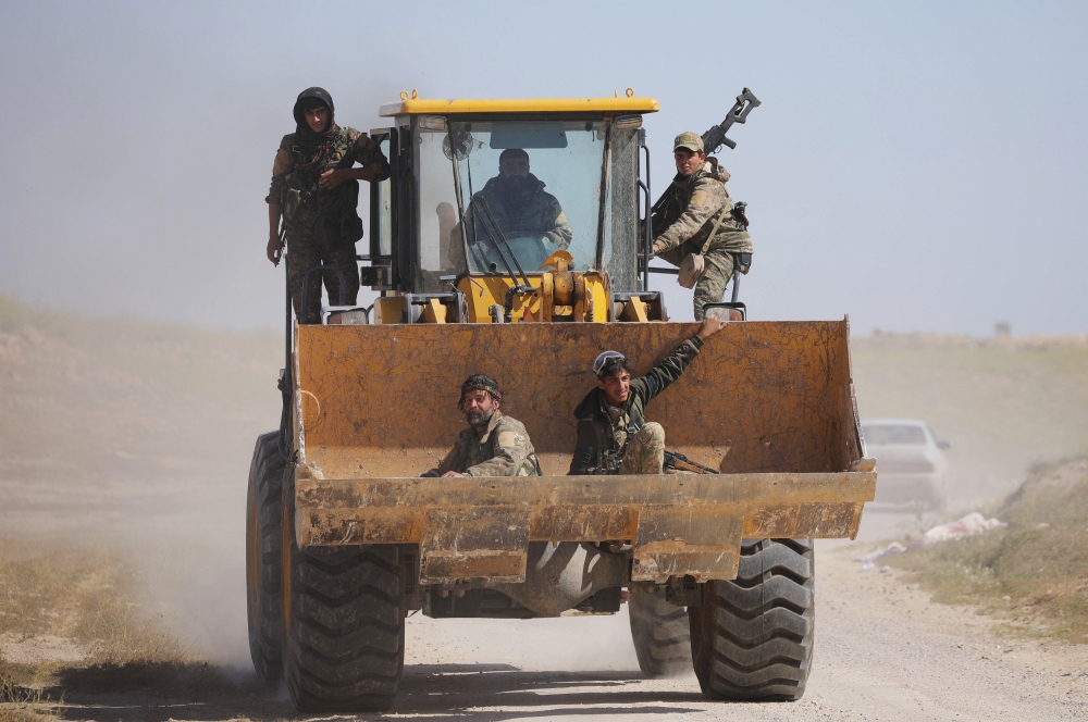 Fighters from the Syrian Democratic Forces (SDF) sit in the bucket of an excavator in the village of Baghouz, Deir Al Zor province, Syria March 20, 2019. Picture taken March 20, 2019. REUTERS/Rodi Said