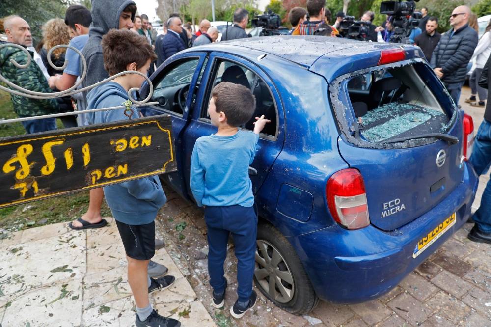 TOPSHOT - People gather around a damaged car next to a house that was damaged after it was hit by a rocket in the village of Mishmeret, north of Tel Aviv on March 25, 2019. A rocket hit a house in a community north of Tel Aviv and caused it to catch fire on Monday, wounding five Israelis, police and medics said. / AFP / Jack GUEZ
